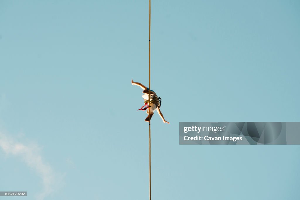 Low angle view of man slacklining against clear blue sky during sunny day