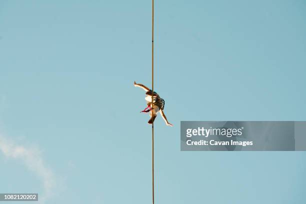 low angle view of man slacklining against clear blue sky during sunny day - corda bamba - fotografias e filmes do acervo