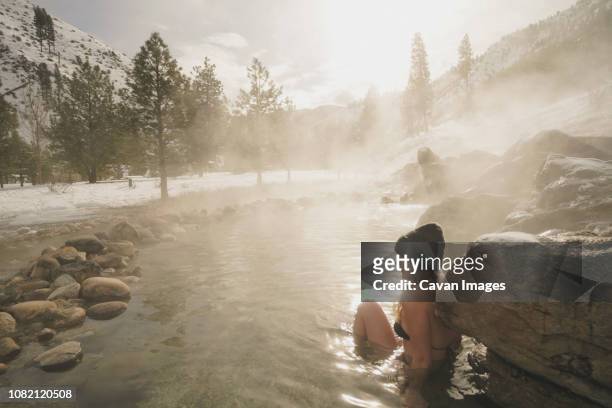 side view of woman wearing bikini while sitting in thermal pool at forest during winter - hot spring stock pictures, royalty-free photos & images