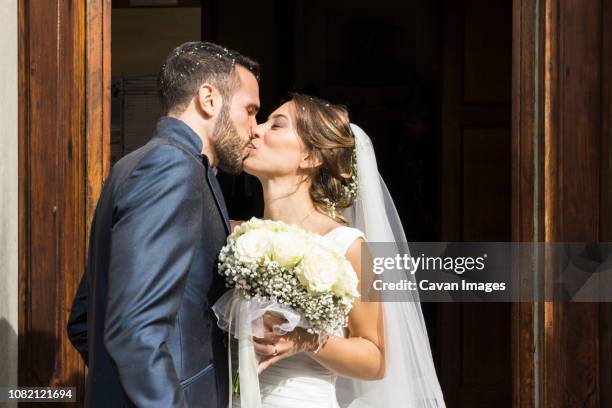 newlywed couple kissing while standing at church entrance - married church stock pictures, royalty-free photos & images