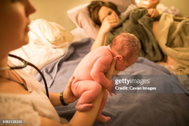 midwife holding newborn baby girl while mother lying on bed at home - home birth stock-fotos und bilder