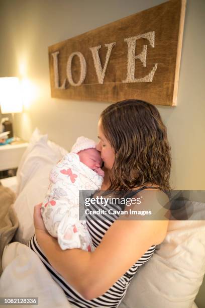 mother kissing newborn daughter while sitting on bed at home - home birth stock-fotos und bilder