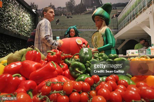 Stand hostesses dressed as garden vegetables stand next to fresh vegetables on display at the Netherlands hall at the 2011 Gruene Woche agricultural...