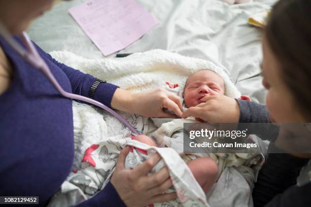 high angle view of midwife examining newborn baby girl by woman on bed at home - home birth stock-fotos und bilder