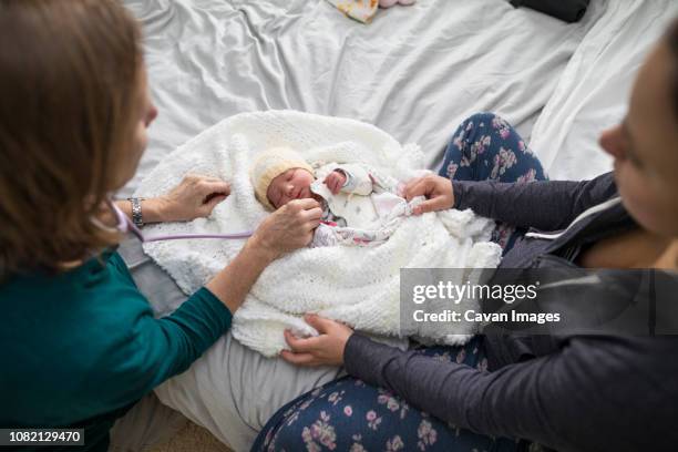 high angle view of midwife examining newborn baby girl while mother sitting on bed at home - comadrona fotografías e imágenes de stock
