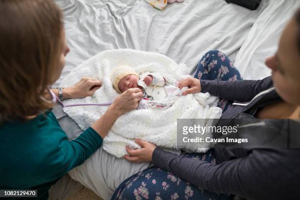 high angle view of midwife examining newborn baby girl while mother sitting on bed at home - home birth - fotografias e filmes do acervo