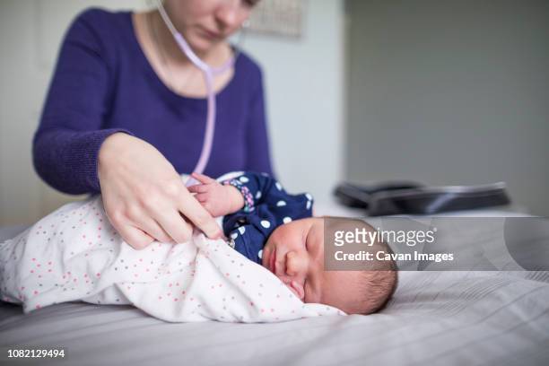 midwife examining newborn sleeping baby girl with stethoscope on bed at home - home birth 個照片及圖片檔