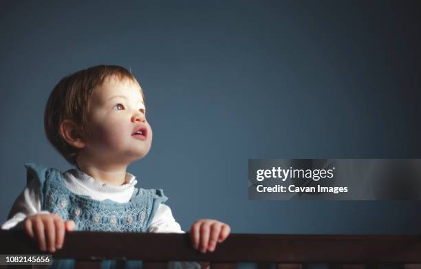 cute baby girl looking away while standing in crib against wall at home - child standing stock pictures, royalty-free photos & images