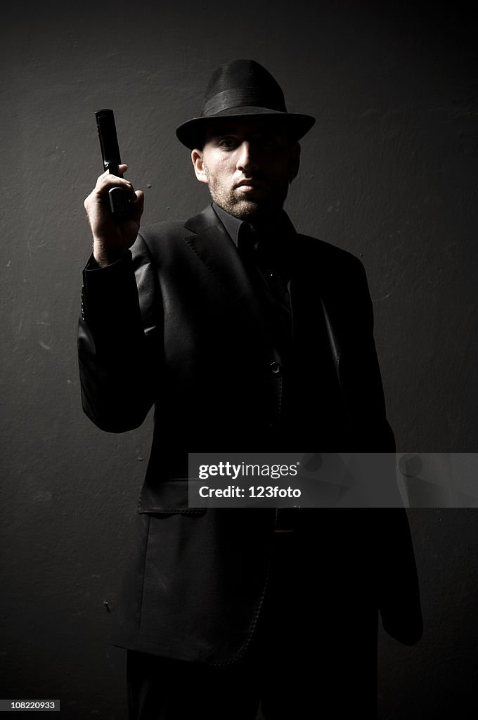 Homem vestindo Terno e Chapéu preto segurando a arma