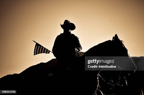 silhouette of cowboy on horse holding american flag - holding horse stockfoto's en -beelden