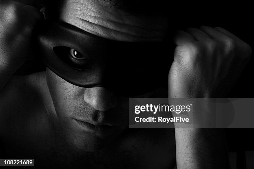 Man in the dark putting on a mask over his eyes Man in the dark putting on a mask over his eyes