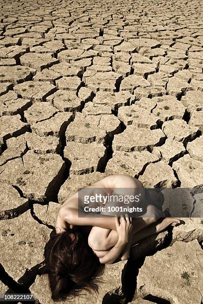 naked young woman curled up on arid desert soil - woman curled up stock pictures, royalty-free photos & images