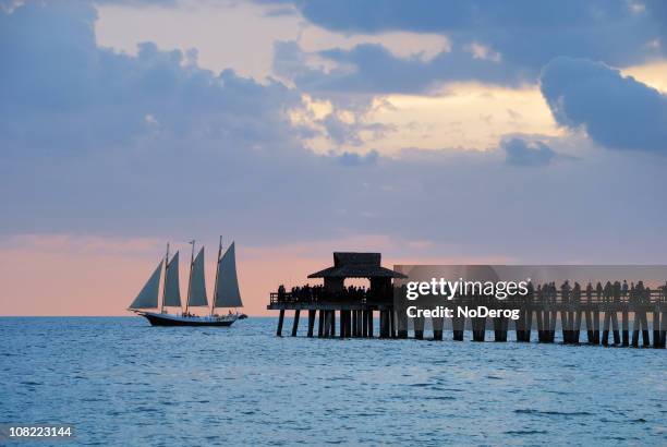 pier with passing sailboat at dusk - naples florida stock pictures, royalty-free photos & images