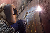 Worker in protective gear welding new plates on ship's hull.