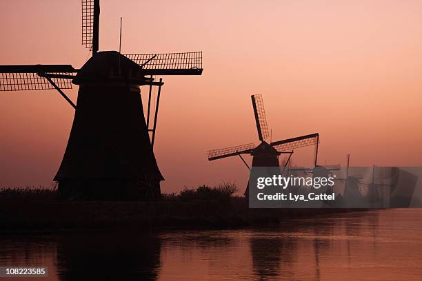 silhouette of windmills on water at sunrise - mill bank stock pictures, royalty-free photos & images