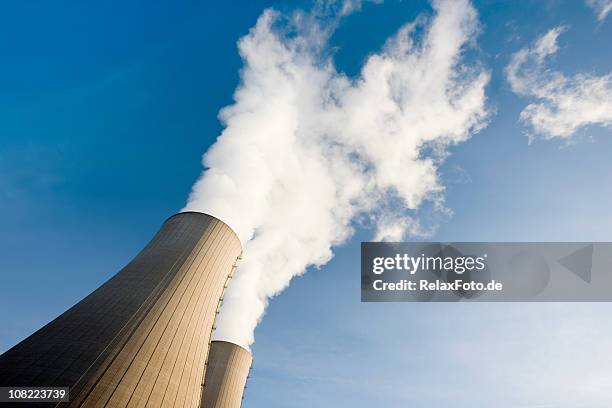 tilt shot of two steaming cooling towers with blue sky - kärnkraftverk bildbanksfoton och bilder