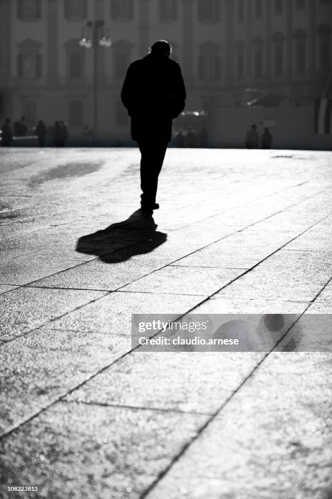 Silhouette of Man Walking Through Town Square. Black and White