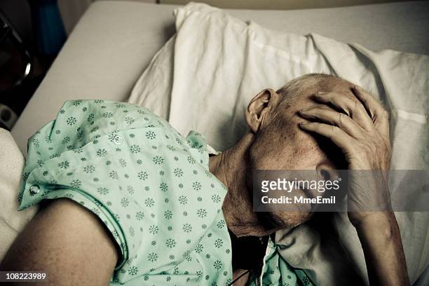 sick and senior man wearing hospitable gown lying in bed - cancer illness stock pictures, royalty-free photos & images