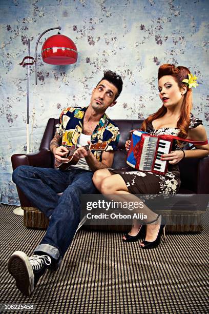 rockabilly couple playing ukelele and accordion on couch - rockabilly pin up girls stock pictures, royalty-free photos & images
