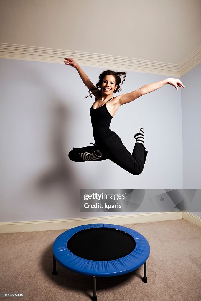 Young woman gymnast on a trampoline in a room