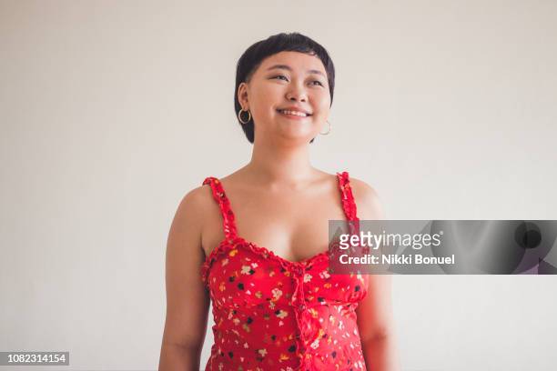 young woman standing in front of a white wall while smiling and looking away - beautiful filipino women stock pictures, royalty-free photos & images