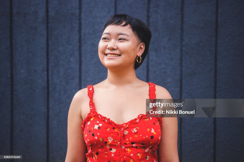 Young woman standing in front of blue wall while smiling and looking away