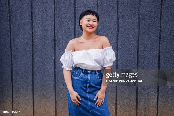 young woman standing in front of blue wall smiling while looking at camera - beautiful filipino women stock pictures, royalty-free photos & images