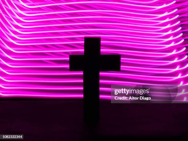 cross shape in a dark environment with a background formed by purple horizontal lines. oneiric atmosphere. light painting. conceptual nature - online church stock pictures, royalty-free photos & images