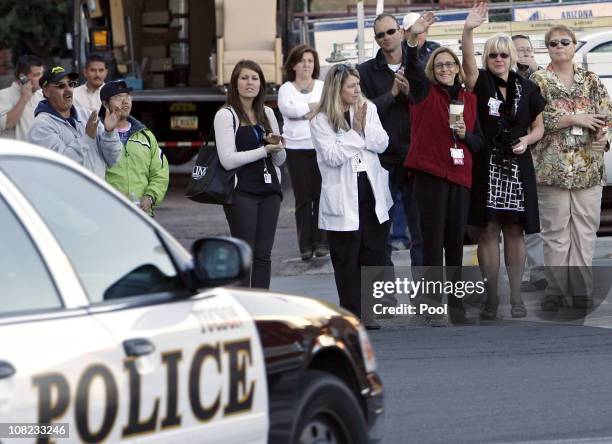 Hospital staff and others wave as a convoy of cars follows the ambulance carrying Rep. Gabrielle Giffords leaves University Medical Center behind a...