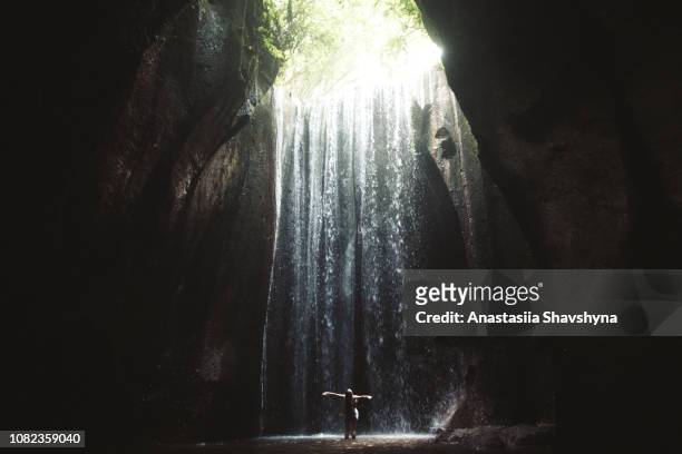 woman staying under hidden waterfall in cave on bali - bali waterfall stock pictures, royalty-free photos & images