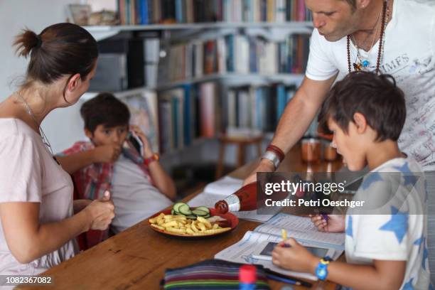 a family snacking on potato chips while sitting around the table at home. - family eating potato chips stock pictures, royalty-free photos & images