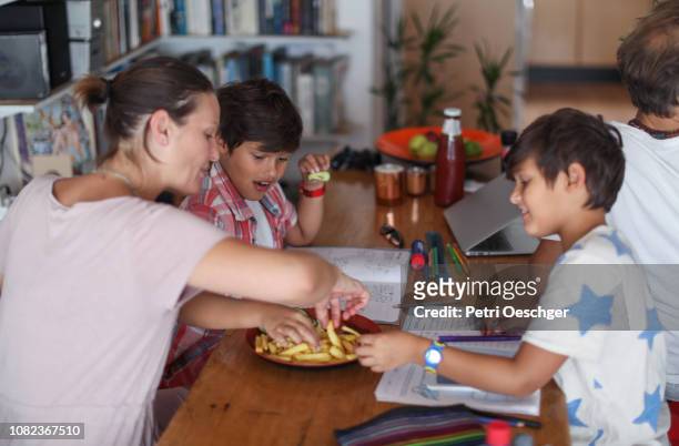 a family snacking on potato chips while sitting around the table at home. - family eating potato chips stock pictures, royalty-free photos & images