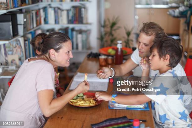 a family snacking on potato chips while sitting around the table at home. - family eating potato chips stock pictures, royalty-free photos & images