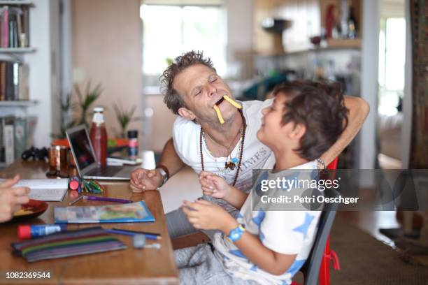 a family snacking on potato chips while sitting around the table at home. - playful joking home stock pictures, royalty-free photos & images