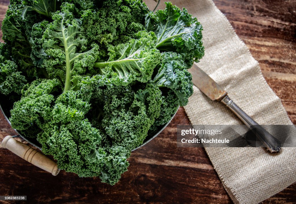 Kale in basket and knife on wooden  background top view on daylight superfood vegetables