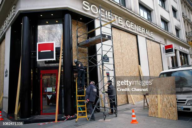Workers install wood panels to protect the facade of the Societe Generale bank against possible damage on the eve of a demonstration of "Yellow...