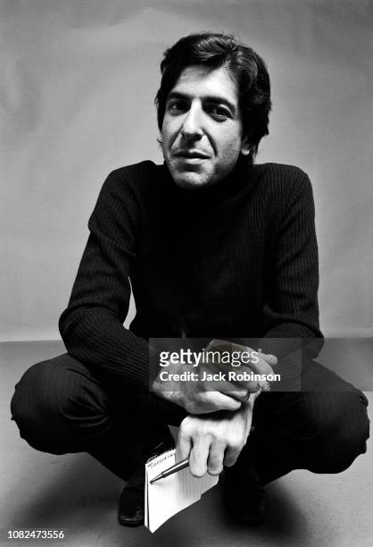 Portrait of Canadian poet, novelist, and musician Leonard Cohen , dressed in black, as he crouches down, a cigarette in one hand and a notebook and...
