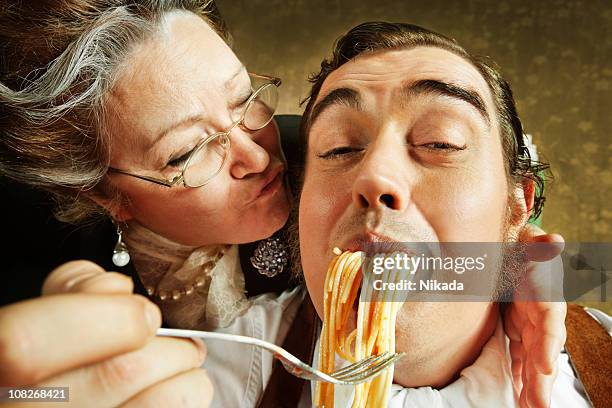 overzealous mother feeding adult son pasta - eating pasta stock pictures, royalty-free photos & images