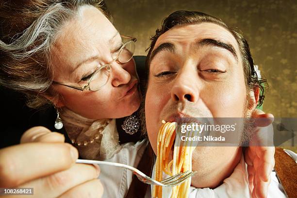 overzealous mother feeding adult son pasta - cuisine humour stock pictures, royalty-free photos & images