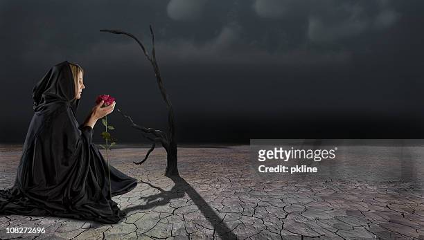 cloaked woman holding flower in barren desert - robe rose stock pictures, royalty-free photos & images
