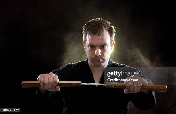 karate man holding nunchucks on black background - nunchucks stock pictures, royalty-free photos & images