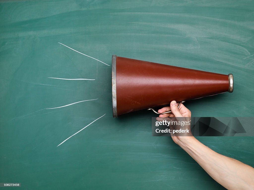 A brown megaphone in front of a green chalkboard with lines
