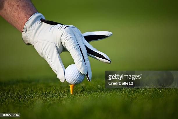 man's hand wearing glove placing golf ball on tee - putting gloves stock pictures, royalty-free photos & images
