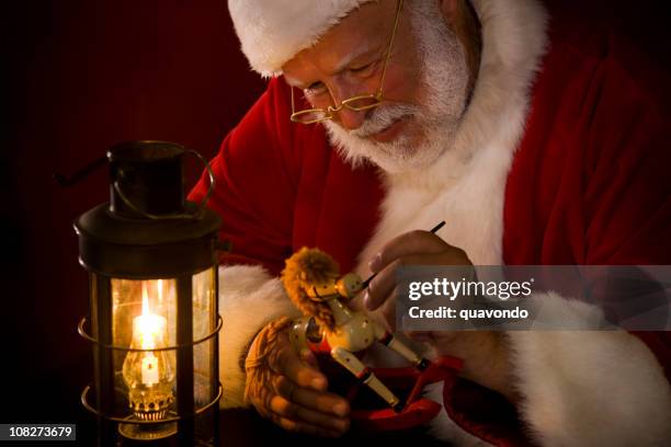 antique image of santa claus painting toy by lantern light - santas workshop stock pictures, royalty-free photos & images