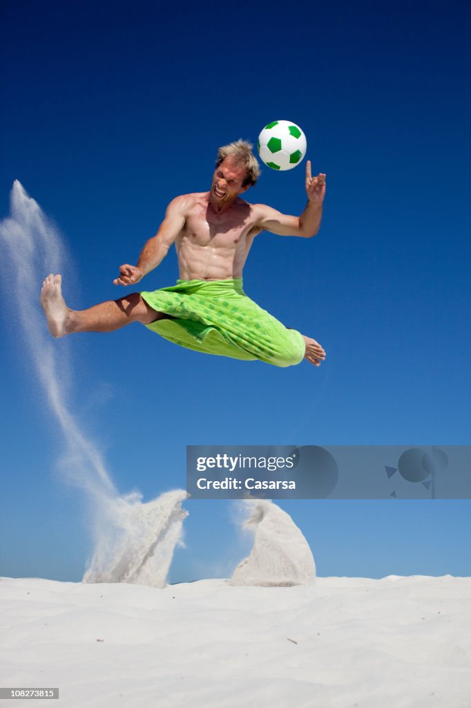 Young Man Jumping and Playing Soccer on Beach