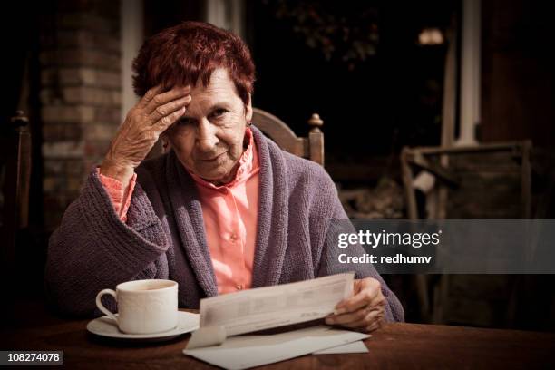 an elderly lady sat looking stressed reading bills - debt collector stockfoto's en -beelden