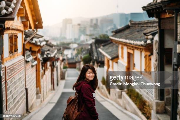 young woman traveler traveling into bukchon hanok village at seoul city, south korea. bukchon hanok village is home to hundreds of traditional houses. - south stock-fotos und bilder