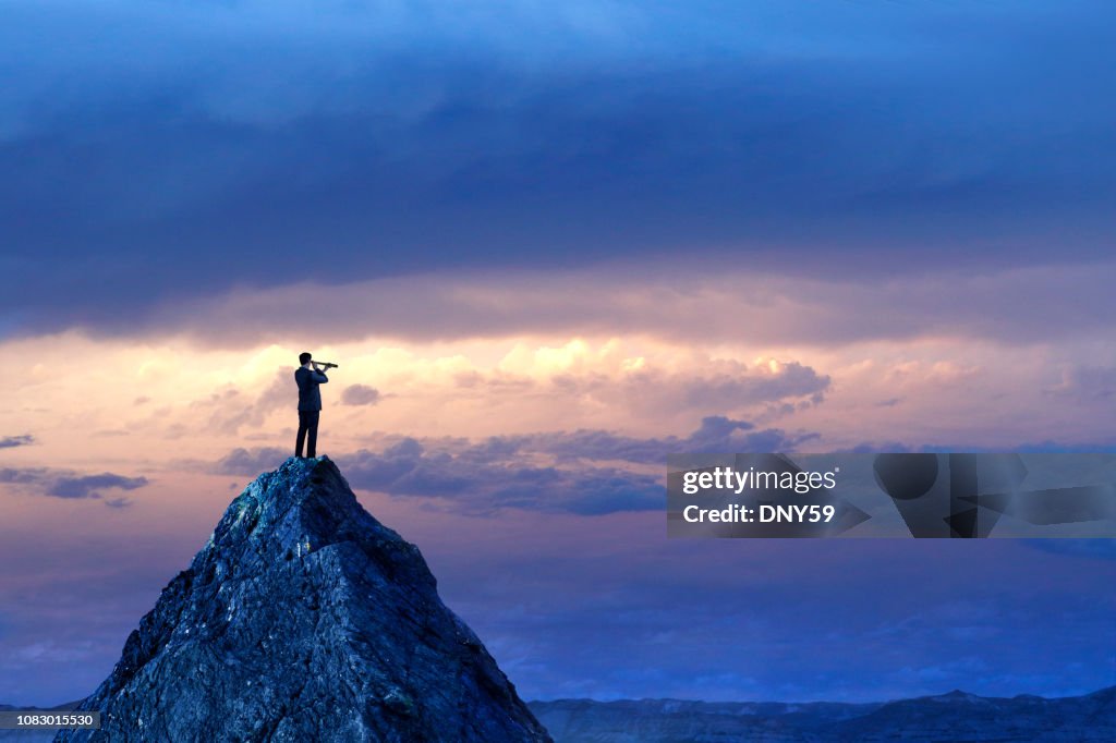 Uomo d'affari in piedi a guardare attraverso Spyglass sulla vetta della montagna