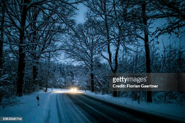 Car drives with dipped headlights through a snowy forest during blue hour on January 11, 2019 in Koenigshain, Germany.
