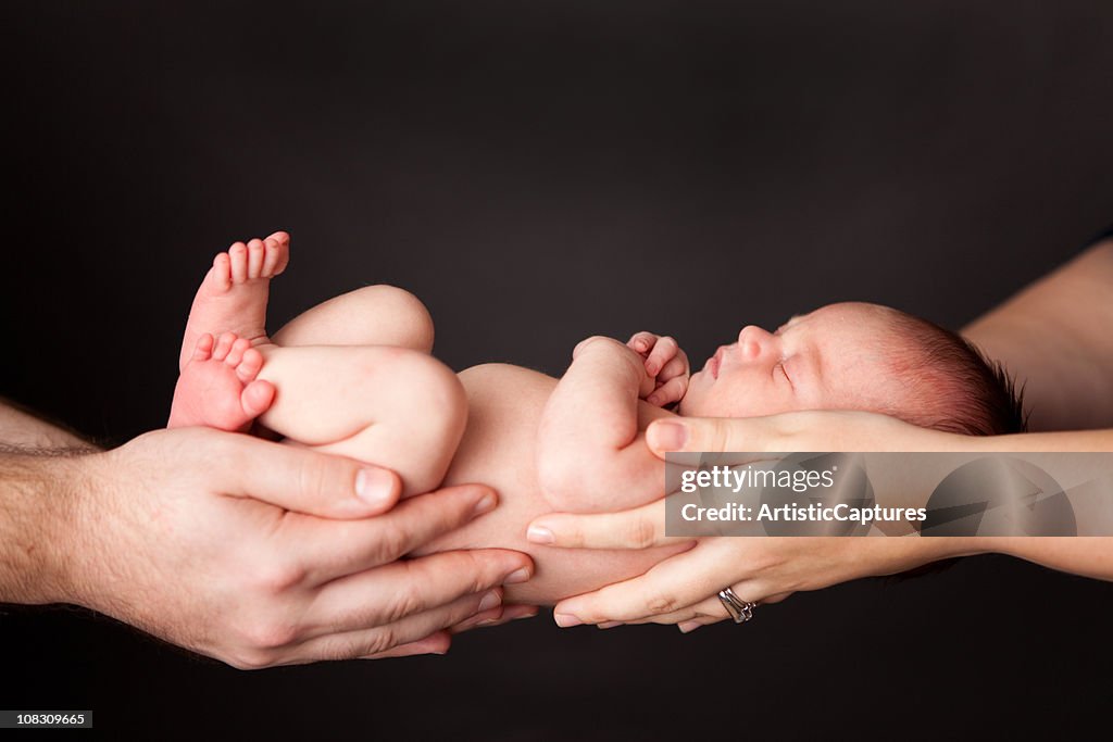 Hands of Father and Mother Holding Newborn Baby